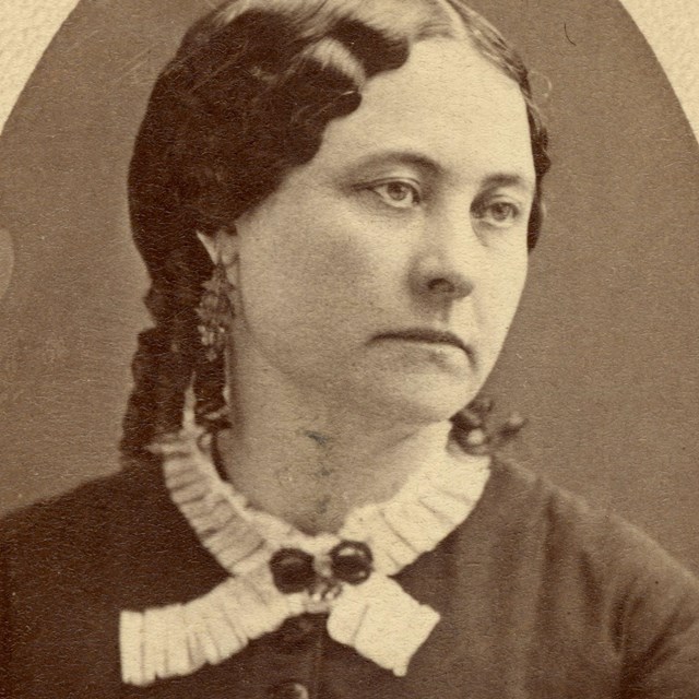 A woman with dark hair and dark colored dress with a lace collar.