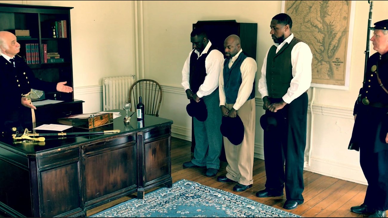 Reenactment of Butlers Interview with Contrabands Five men in a historically furnished office reenact a meeting between escaped slaves and military officers.